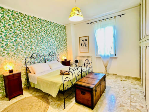 Camera luminosa in Agriturismo CasaViVa con carta da parati floreale, letto in ferro battuto, illuminazione gialla e vista sul giardino