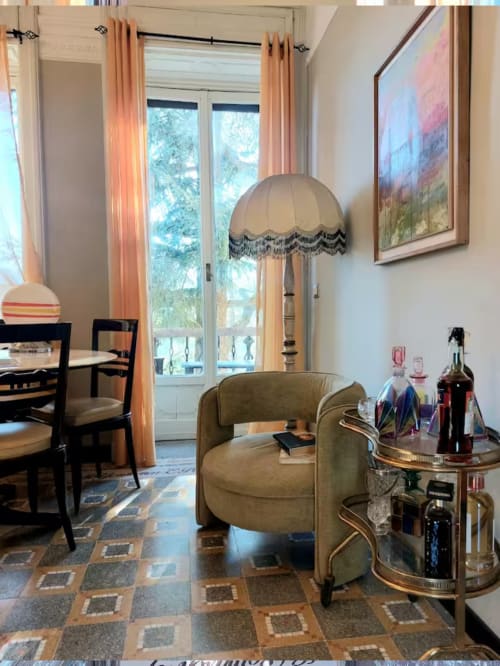 Élégant salon du Palazzo Losio à Ponzone avec fauteuil olive, lampadaire et vue sur le jardin par de grandes fenêtres