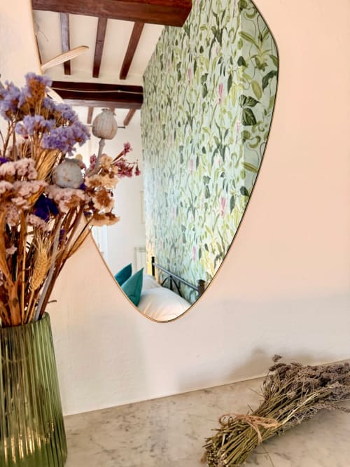 Specchio ovale con cornice in ottone che riflette carta da parati floreale, fiori secchi in vaso verde, arredamento camera CasaViVa