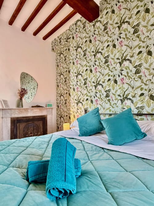 Bedroom at Agriturismo CasaViVa with twin beds, turquoise pillows, floral wallpaper, exposed beams, and fireplace