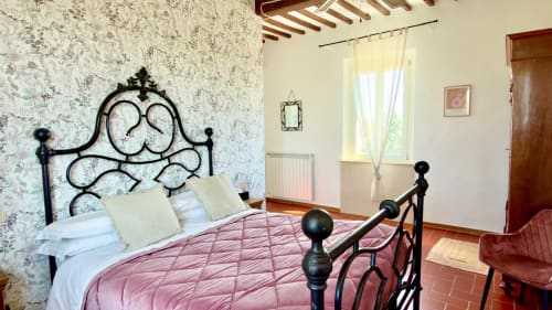 La camera Profumo dell'Agriturismo CasaViVa con letto in ferro battuto, coperta trapuntata rosa e vista sul giardino in Toscana
