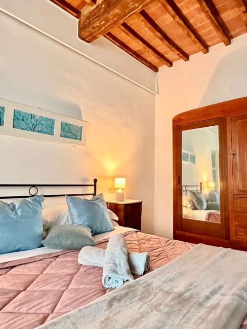 Bright bedroom at Agriturismo CasaViVa with exposed wooden beams, blue pillows, and wooden-framed mirror door