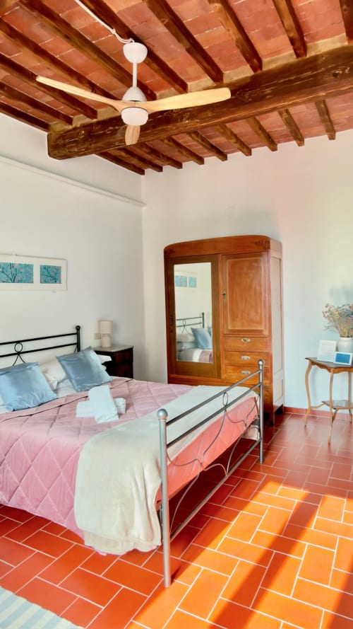 Camera rustica ad Agriturismo CasaViVa con travi in legno a vista, pavimento in cotto e letto in ferro battuto con blu