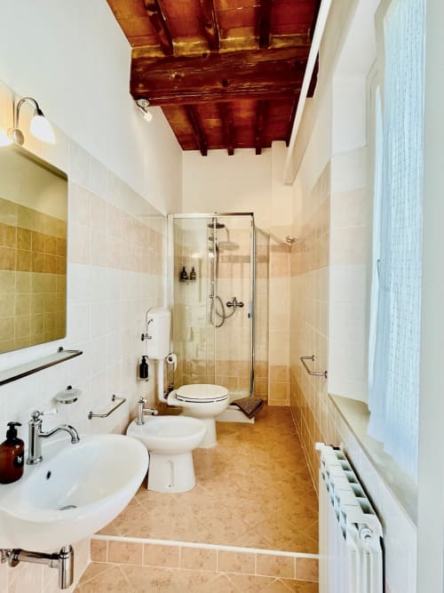 Bagno moderno con doccia piastrellata, doppi lavabi e travi in legno a vista presso l'Agriturismo CasaViVa a Pozzo della