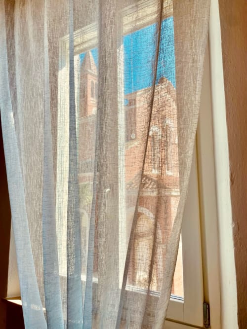 Tende trasparenti incorniciano il campanile in mattoni della chiesa sotto il cielo azzurro di Agriturismo CasaViVa a Pozzo della Chiana