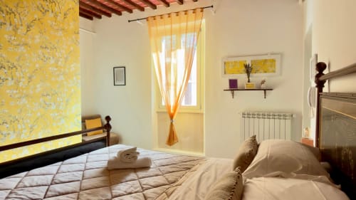 Camera luminosa in Agriturismo CasaViVa con carta da parati a fiori gialli, letti gemelli, finestra con tende arancioni e stile rustico