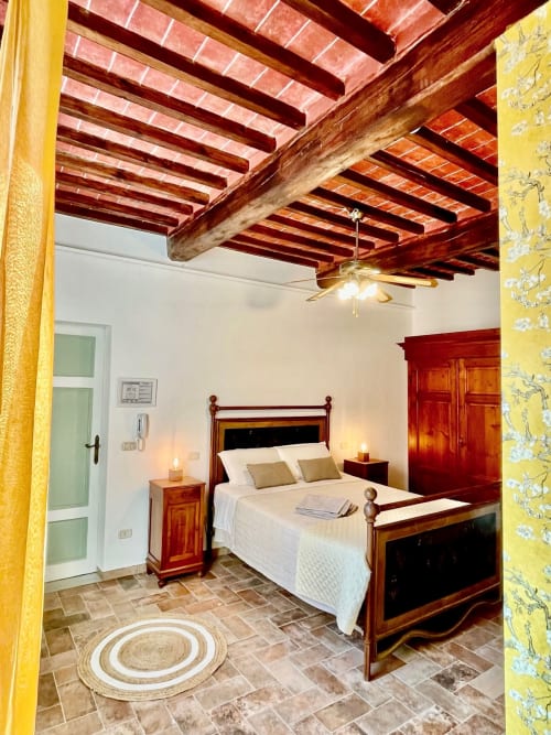 Bedroom at Agriturismo CasaViVa with wooden beamed ceiling, terracotta floors, wooden bed, yellow walls, and rustic Italian