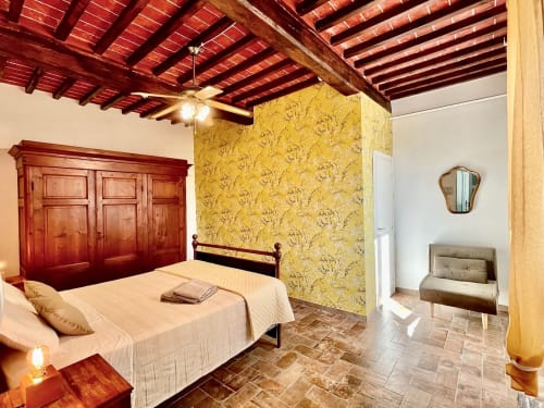 Camera rustica all'Agriturismo CasaViVa con armadio in legno rosso, pareti con carta da parati gialla, pavimenti in cotto e travi esposte