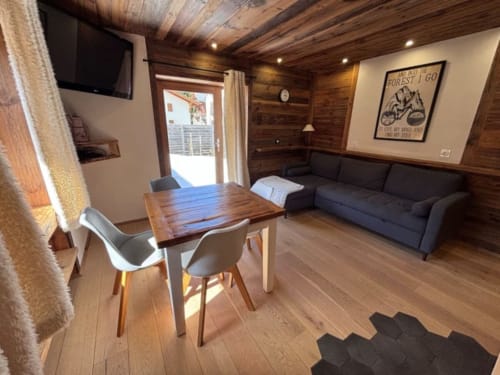 Intérieur de chalet moderne Chez Francine avec plafond en bois, canapé sombre, table à manger et vue sur les montagnes à Notre-Dame-de