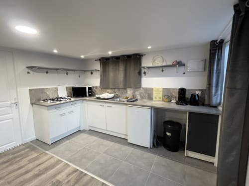 Cuisine moderne du studio Les Oiseaux à Sanateflo, Rai : mobilier blanc, plan de travail gris et électroménagers inox.