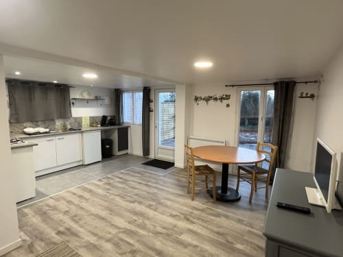 Cuisine ouverte et coin repas du studio Les Oiseaux à Raï avec mobilier blanc, table ronde et vue sur le jardin