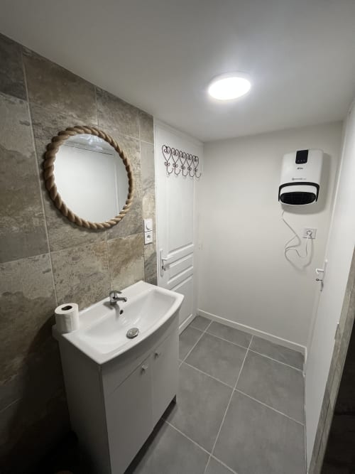 Salle de bains moderne de l'appartement Sanateflo avec lavabo, miroir en corde, radiateur mural chauffant et carrelage gris