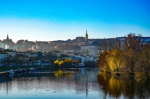 Vue pittoresque de Bourg-Charente au bord de l'eau : architecture historique, clocher d'église et arbres d'automne dorés reflétés dans l'eau calme