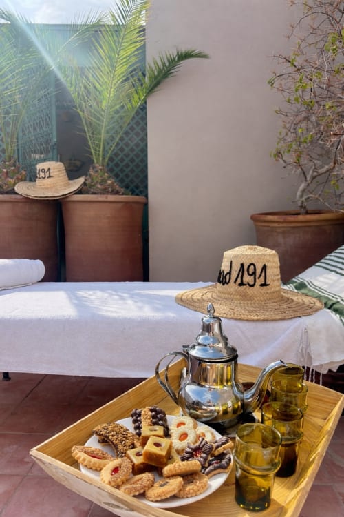 Service de thé à la menthe et pâtisseries dans la cour du Riad 191, avec théière et chapeaux de paille à Marrakech