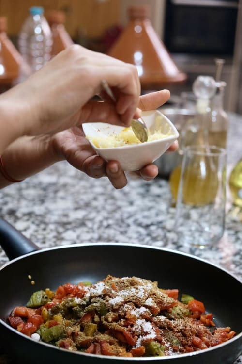 Chef préparant un tajine marocain traditionnel au Riad 191 de Marrakech, assaisonnant les légumes d'épices