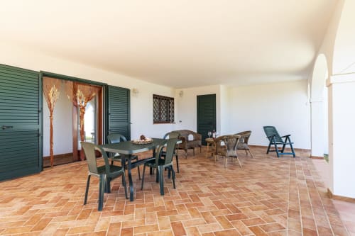 Spacious terracotta-floored veranda at Youinsardinia with dining table, lounge chairs, and garden views in Bari Sardo