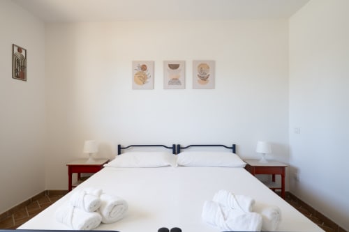Bright modern bedroom with white bedding, dark headboard, twin nightstands with lamps, and boho wall art at Youinsardinia