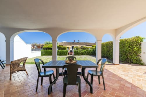 Covered veranda with dining table and chairs overlooking garden at Youinsardinia apartment in Bari Sardo, Italy