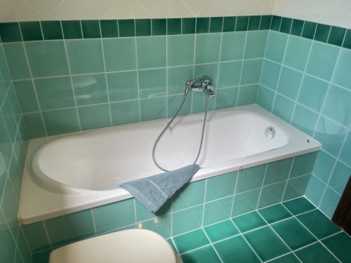 White bathtub with turquoise tile walls and chrome faucet at Like at Home Palau hotel in Palau