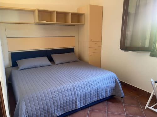 Modern bedroom at Like at Home Palau with blue quilted bedding, wooden storage, and terracotta flooring