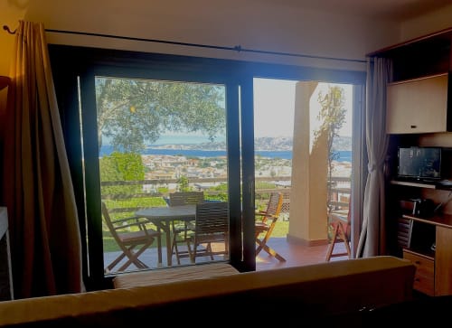Hotel bedroom with blue-framed doors opening to terrace overlooking Palau coastline and Mediterranean Sea view