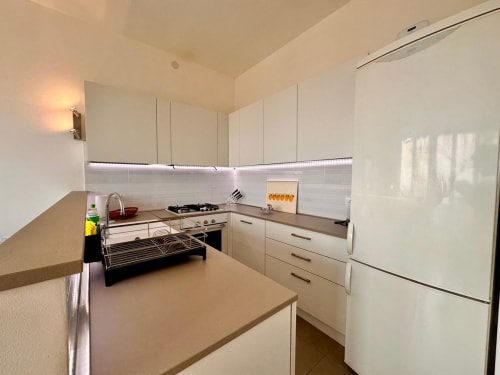 Cucina moderna con mobili bianchi, piano di lavoro beige, fornello a gas e frigorifero a Casa delle Palme, Varigotti