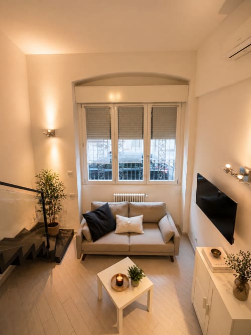 Modern Milan loft with beige sofa, flat-screen TV, city view windows, and minimalist decor - Hb Hall Srl
