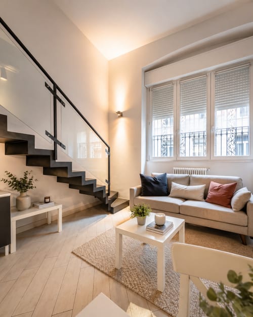 Modern loft in Milano with open-plan living space, black staircase, beige sofa, and city view windows