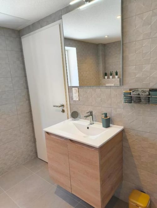 Salle de bain moderne de l'appartement Le Petit Havre de Joy avec vanité en bois, lavabo blanc, grand miroir et murs en carrelage beige