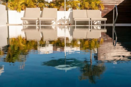 Luxury poolside lounge area at Aevum Resort in Playa del Inglés with white sun loungers and palm trees reflected in crystal