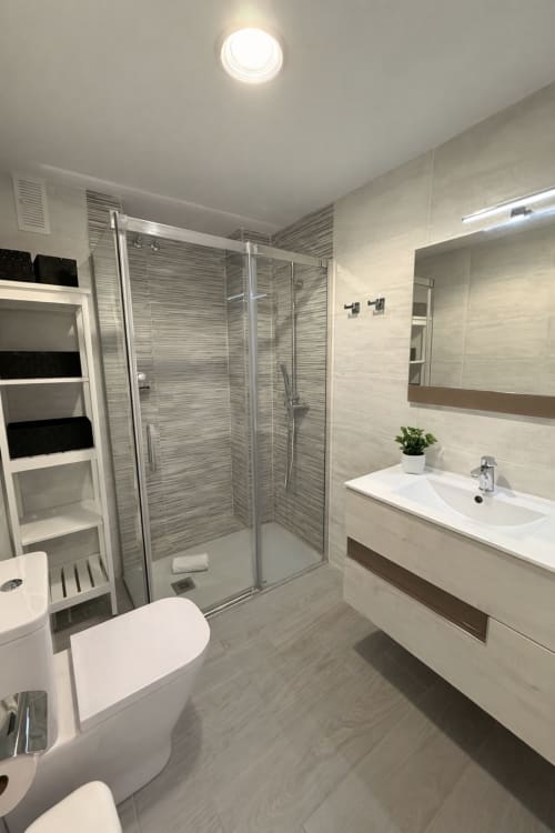 Baño moderno en apartamento de Playa Algarrobo con ducha de cristal, lavabo blanco, inodoro y accesorios cromados en Málaga
