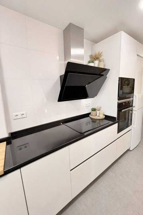 Cocina moderna blanca con encimeras negras, electrodomésticos integrados y campana extractora angular en apartamento de playa en Málaga