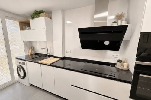 Moderna cocina blanca con encimeras negras, electrodomésticos de acero inoxidable y campana negra en Algarrobo Beach Premium