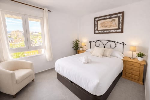 Luminoso dormitorio en apartamento frente al mar de Málaga con vistas al océano, ropa de cama blanca, mesitas de madera y decoración costera