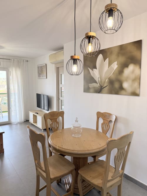 Área de comedor moderna con mesa redonda de madera, sillas, lámparas colgantes, arte mural y TV de fondo en Playa Algarrobo