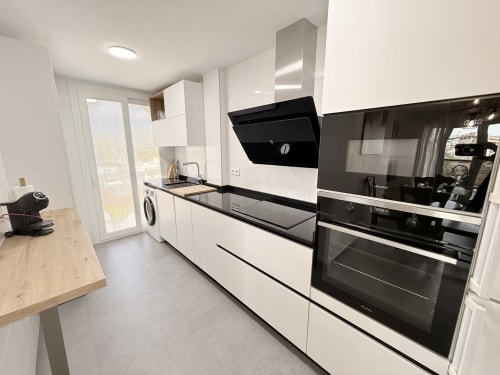 Moderna cocina blanca con encimeras negras, electrodomésticos de acero inoxidable y vistas al mar en apartamento Sinese Design Homes,