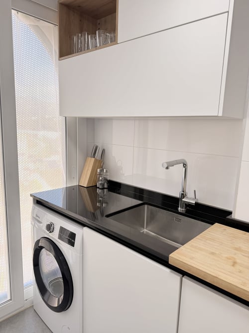 Cocina moderna con fregadero de acero inoxidable, encimera negra, tabla de cortar de madera, bloque de cuchillos y lavadora