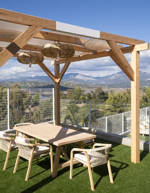 Pérgola de madera con lámparas colgantes tejidas sobre mesa de comedor en terraza con vistas al Embalse de la Viñuela, Málaga