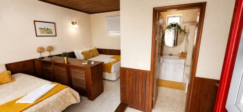 Quarto triplo na Herdade da Cova da Onça com móveis de madeira, detalhes em amarelo e casa de banho privativa com vista para o jardim