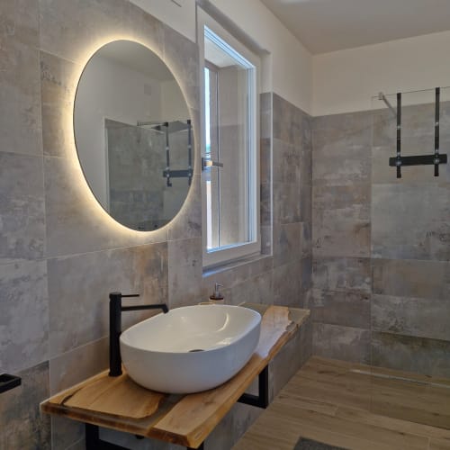 Salle de bain moderne de la résidence Holiday Home Garda Trentino à Arco avec miroir rond rétroéclairé, vasque blanche sur meuble en bois, et