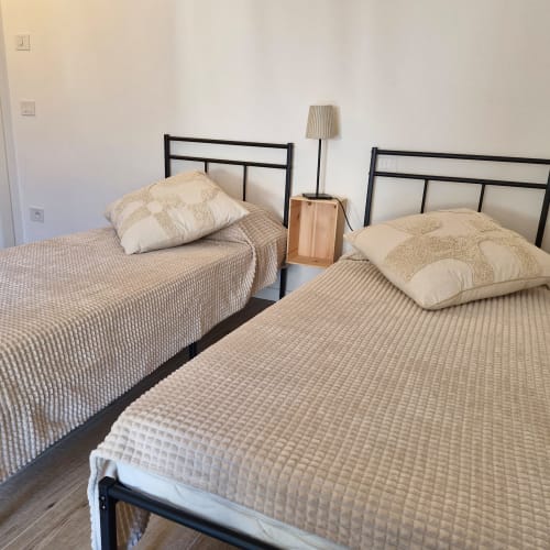 Deux lits simples avec literie crème et cadre en métal noir dans une chambre lumineuse à Holiday Home Garda Trentino, Arco