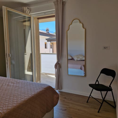 Chambre moderne avec balcon surplombant les montagnes d'Arco, lit, miroir, chaise noire et accès à la terrasse