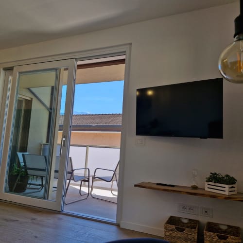 Salon moderne avec téléviseur écran plat, étagère en bois et portes vitrées ouvrant sur une terrasse avec vue montagne à Arco