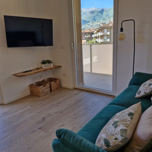 Séjour moderne avec canapé vert, télévision, vue sur les montagnes et balcon donnant sur Arco, Italie