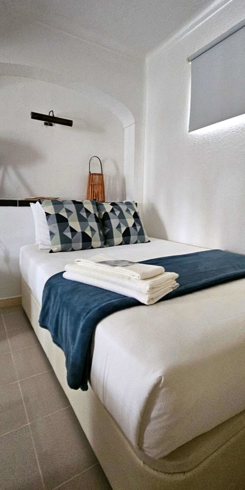 Quarto moderno na Herdade da Cova da Onça com cama branca, almofadas estampadas, manta azul-escuro e design minimalista em Canha