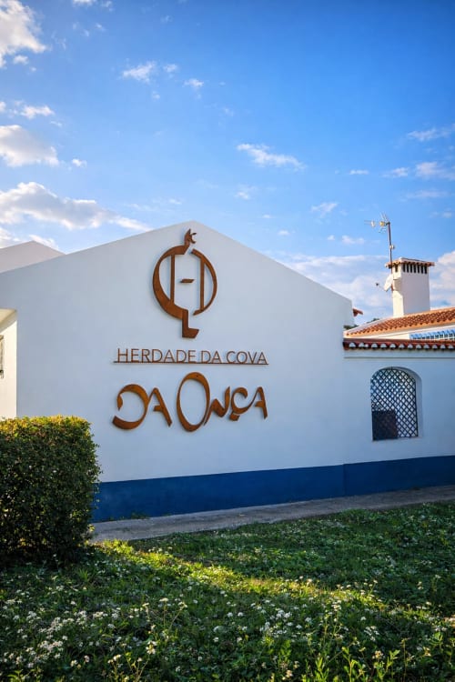 Fachada branca e azul da Herdade da Cova da Onça, boutique hotel em Canha, Portugal, com logo rústico e jardins bem cuidados
