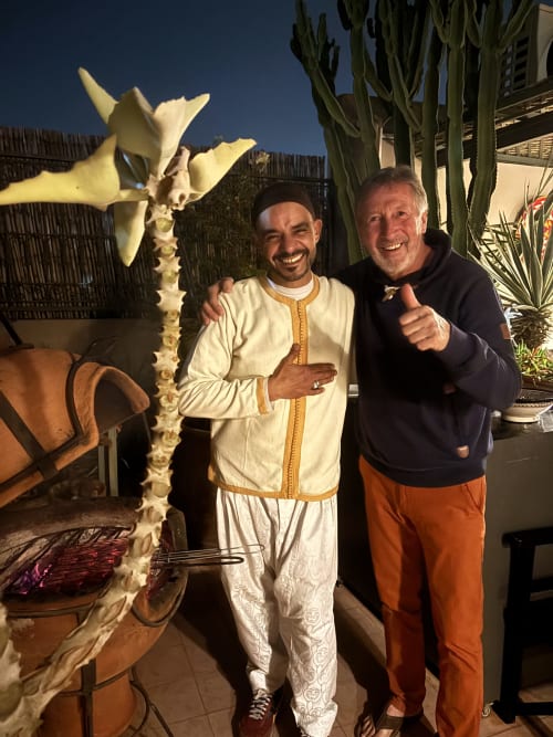 Deux hommes souriants au Riad 191 à Marrakech, l'un vêtu d'une djellaba blanche traditionnelle près d'un cactus décoratif