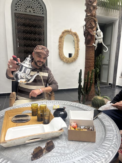 Homme tenant une théière à la table du Riad 191 à Marrakech, décor traditionnel et plantes
