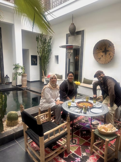 Trois clients dînant à une table ronde dans la cour du Riad 191 à Marrakech, décorée de style marocain avec des plantes
