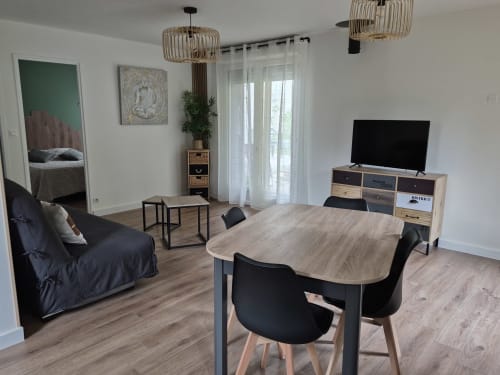 Interior de cabaña moderna de planta abierta en Domaine en Terre Happy con mesa de comedor, sillas negras, mueble para TV, sofá y jardín